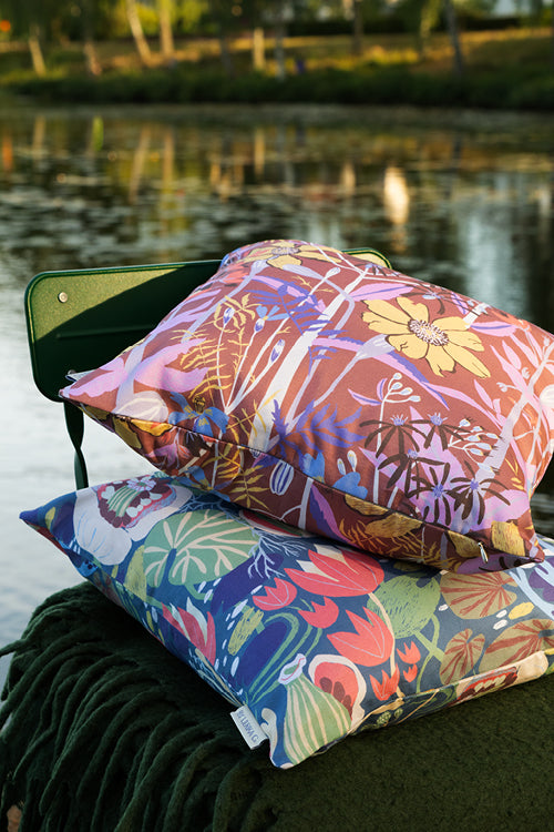 Två mönstrade blommiga kuddar ligger på en stol vid sjön svensk design av BY Ulrika G