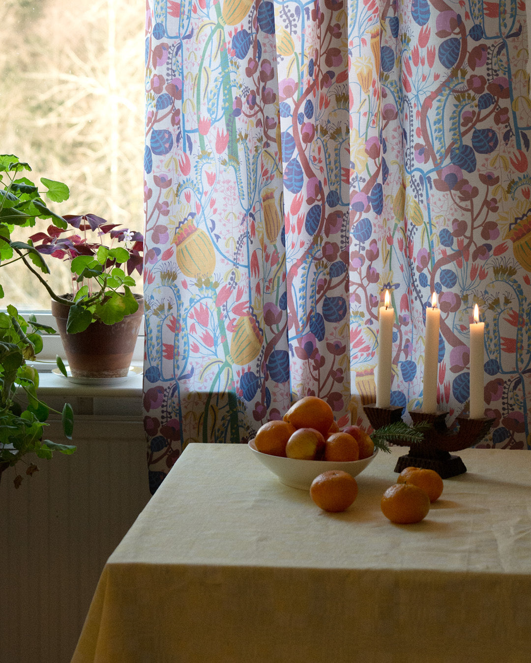 Blommig mönstrad gardin i köket med clementiner och levande ljus