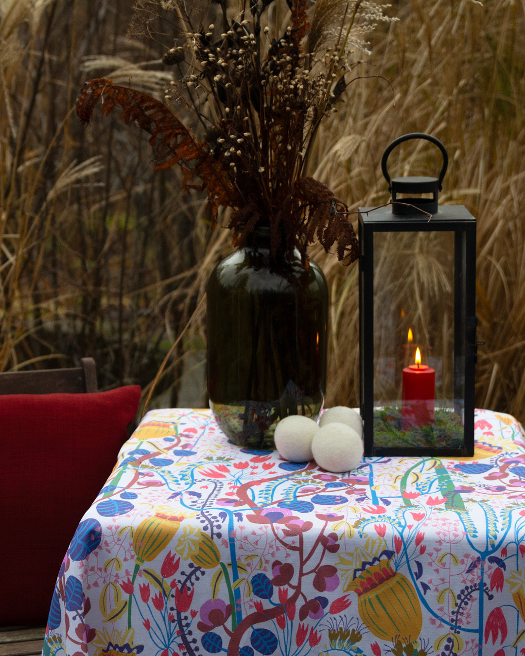 Dukning  en vinter trädgård med vackert gräs, ett bord med blommig mönstrad duk, ljuslykta och vas med blommbukett.