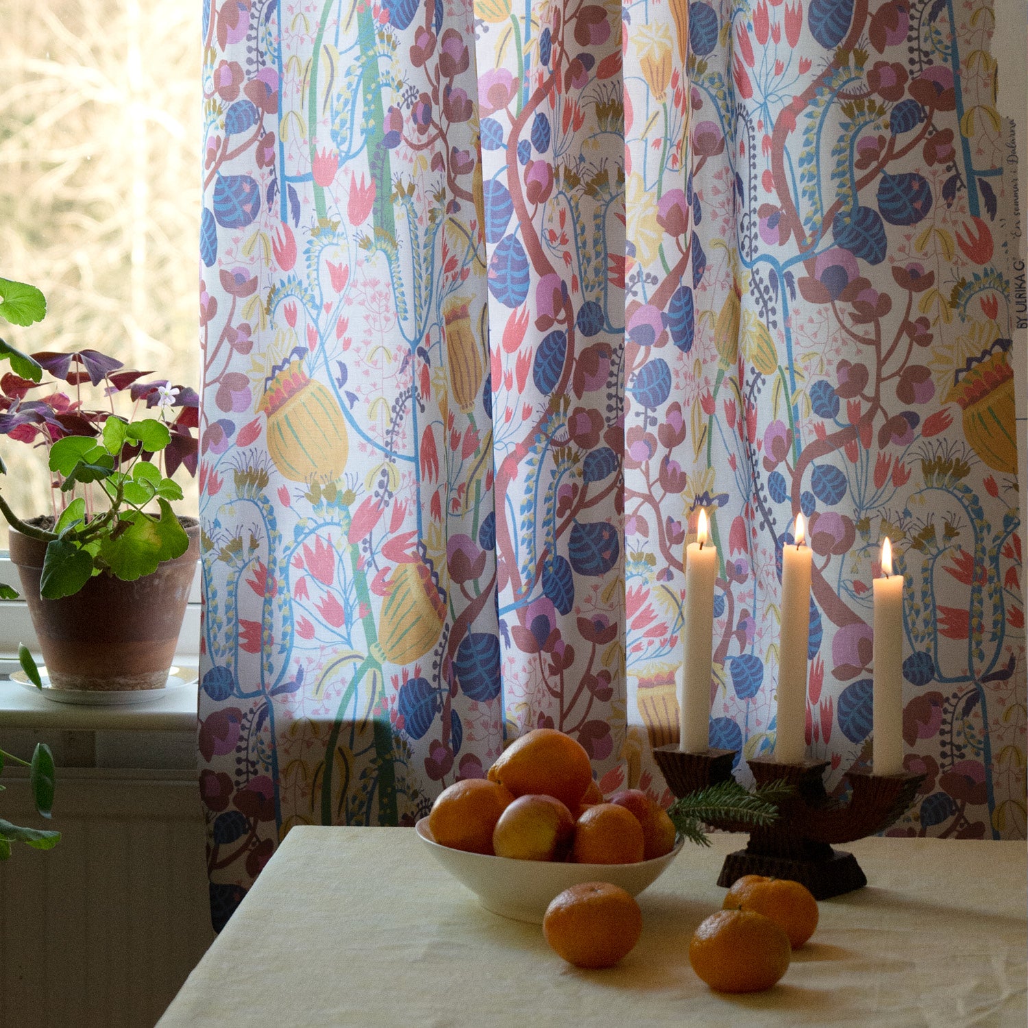 Blommig  mönstrad gardin i köket med clementiner och levande ljus