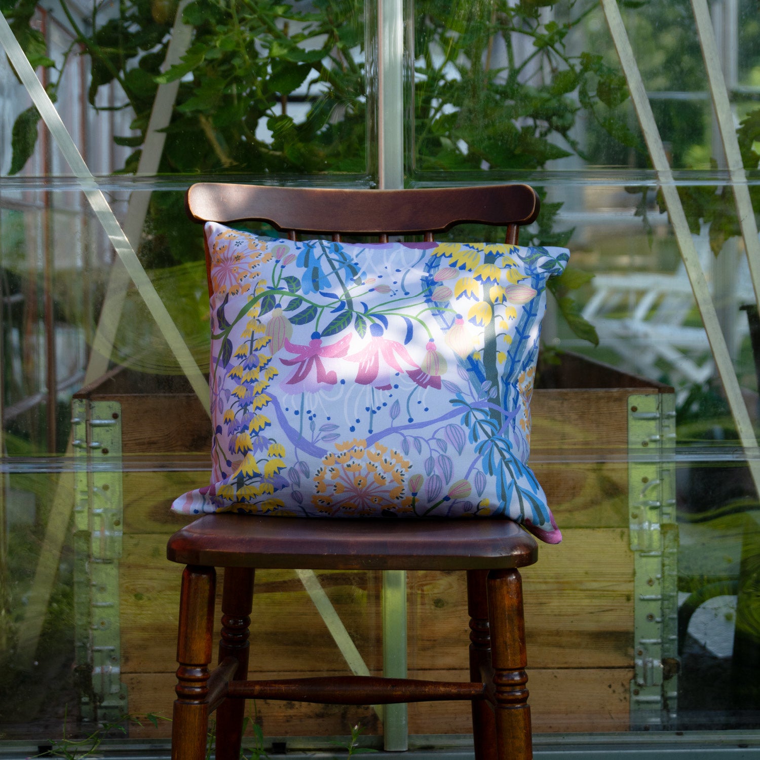 Blommig mönstrad kudde på en stol mot ett växthus