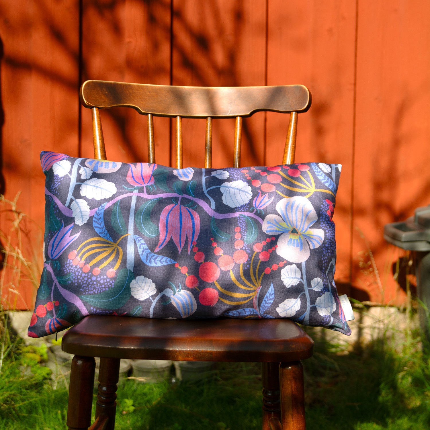 Blommig mönnstrad kudde på en stol mot en röd vägg.