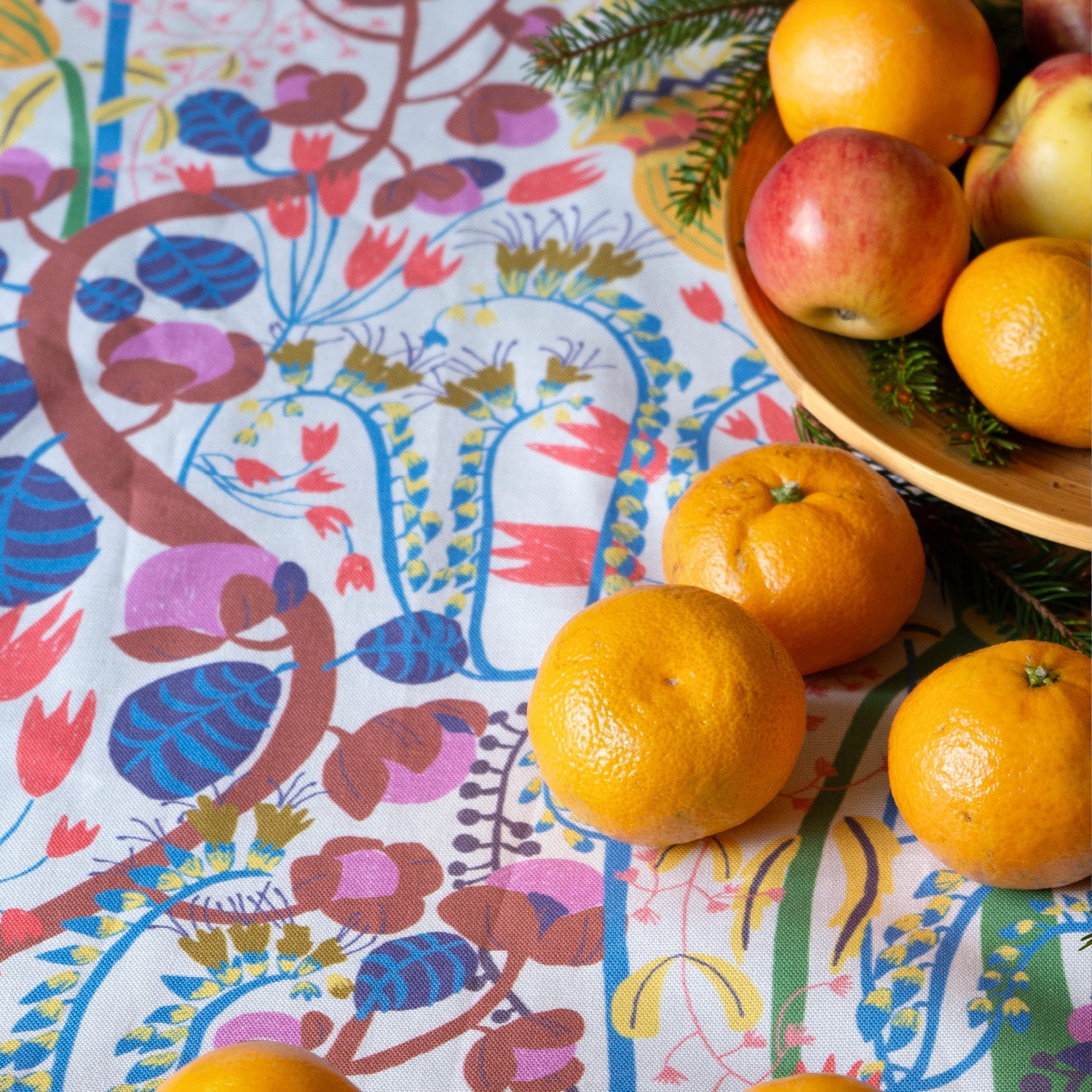 Mönstrat blommigt tyg som duk med clementiner och äpplen i en skål