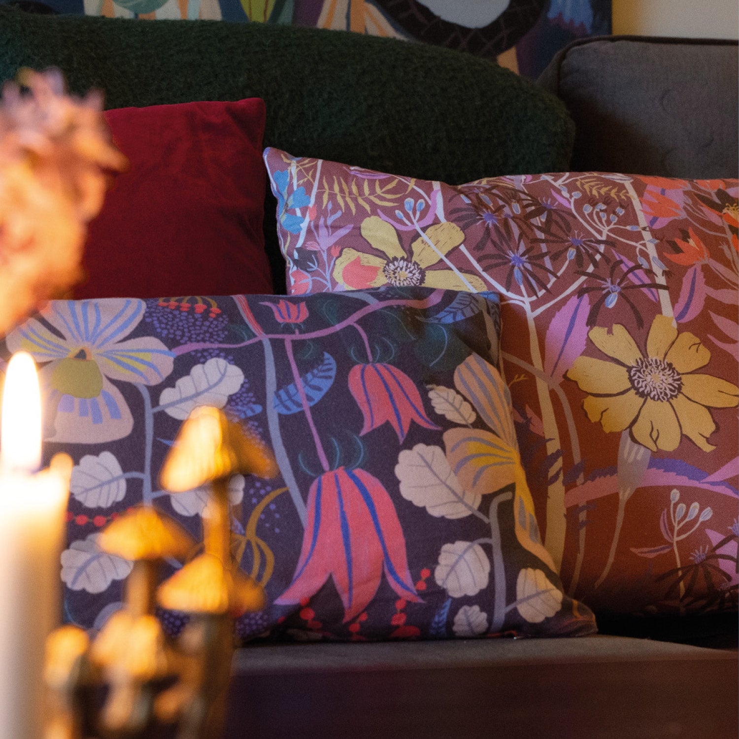 Två blommiga kuddar i soffan  med ljus framför på bordet.