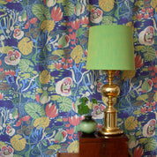 På väggen hänger ett blommigt mönstrat tyg som en gardin i färgerna blå och framför står en grön lampa
