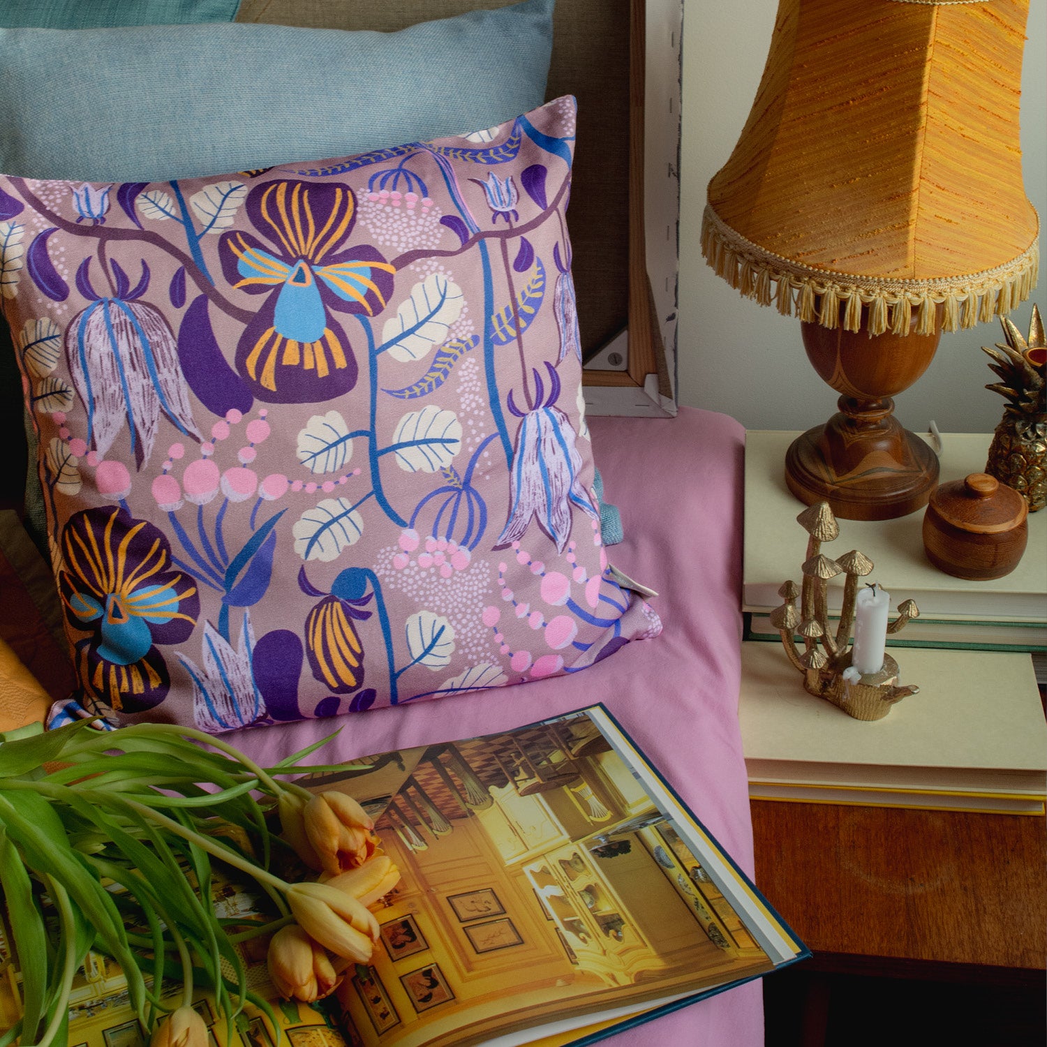 Blommig mönstrad kudde igger i sängen tillsammans med en bok och tulpaner.