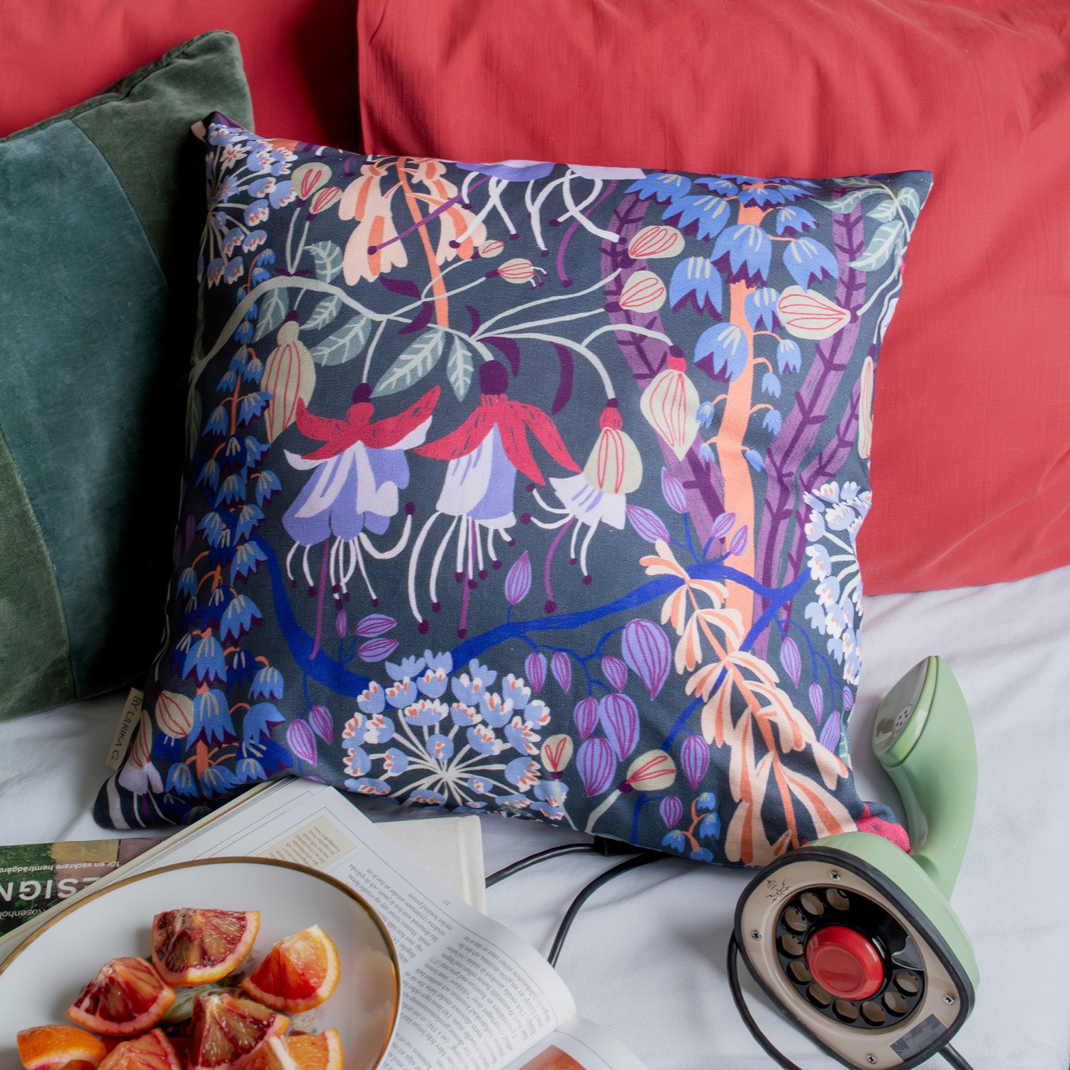 Mend en tlefon och ett fat med apelsiner bredvid ligger en blommig kudde i sängen.