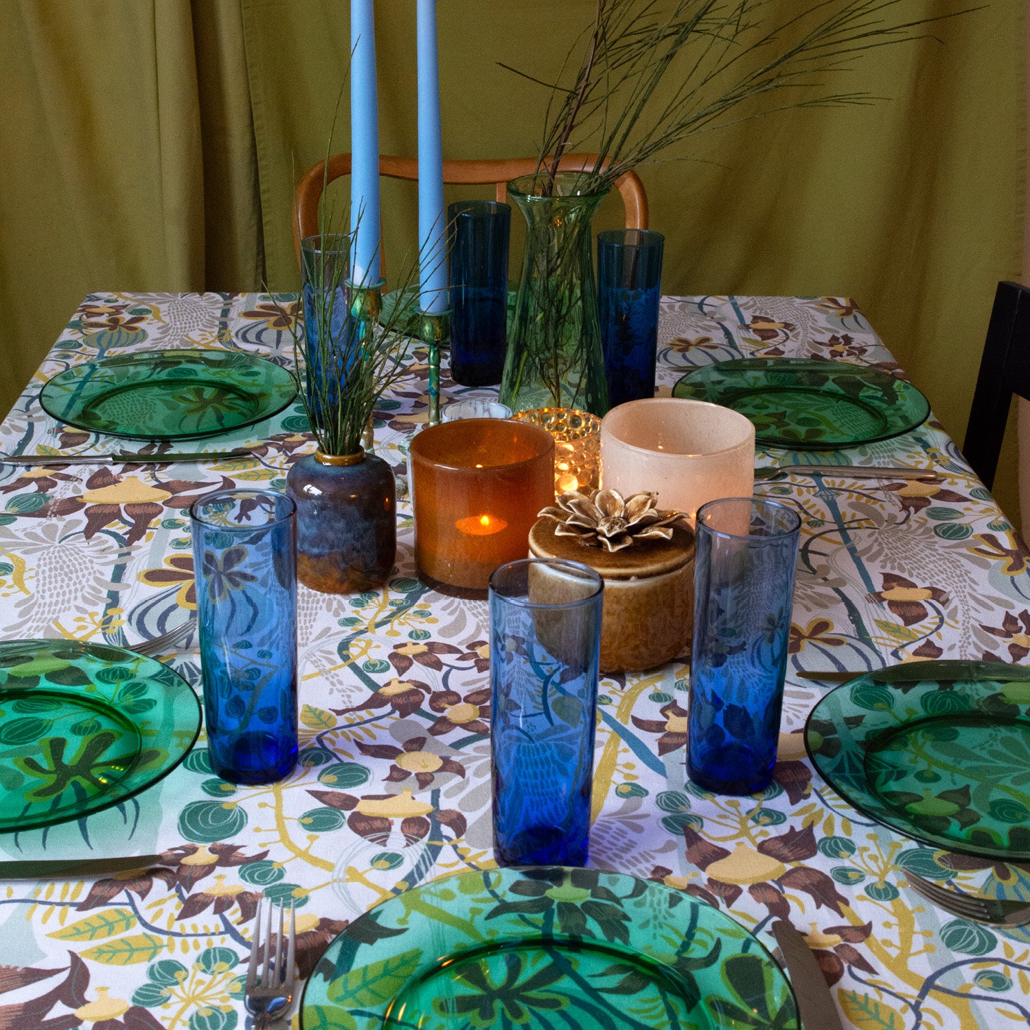 En dukning med gröna tallrikar, blå glas och blommig duk.