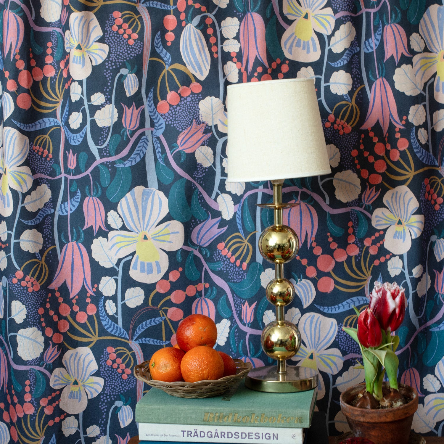 Ett tyg hänger som en gardin  på väggen och framför står en lampa och böcker.