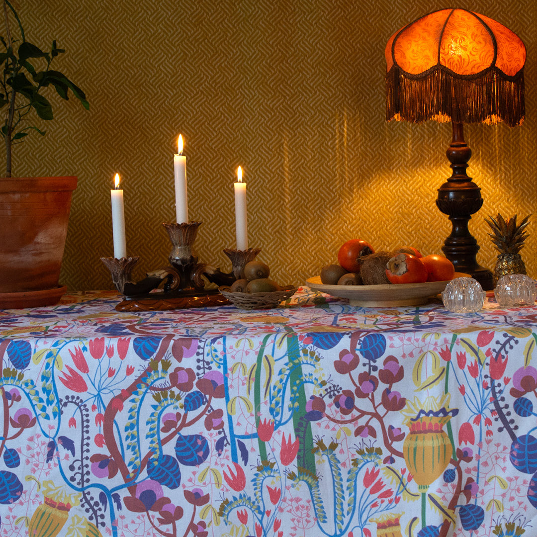 Dukat bord med blommig mönstrad duk, fruktfa, lampa och levande ljus.