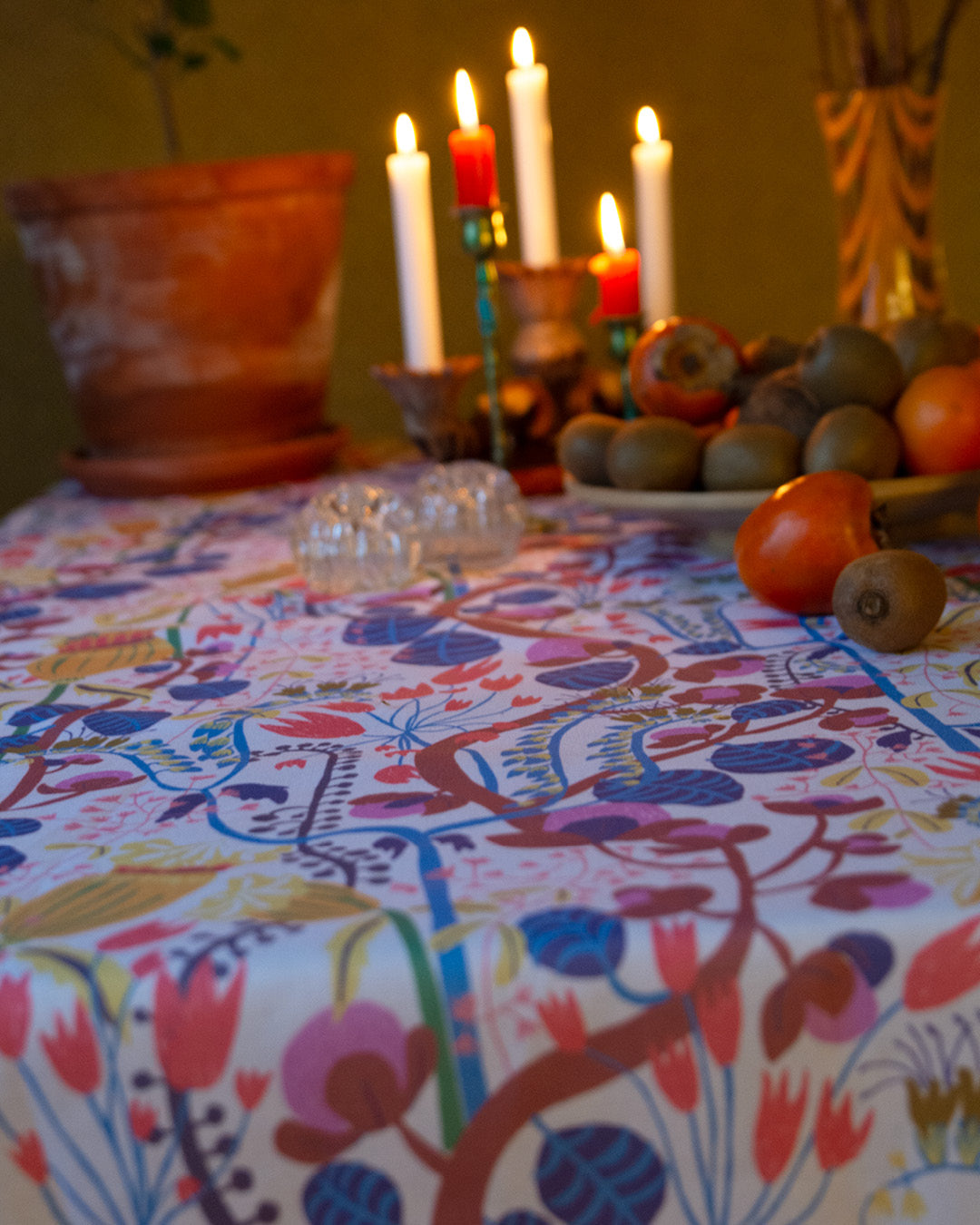 Många levande ljus på ett bord med fruktfat och en blommig duk svensk design av By Ulrika G
