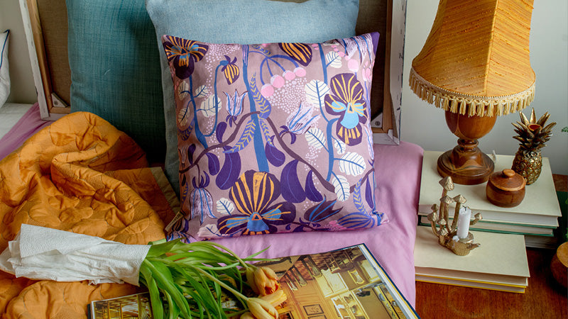 Blommig mönstrad kudde i färgerna brun rosa och blå ligger i sängen tillsamns med en bok och en bukett tulpaner.