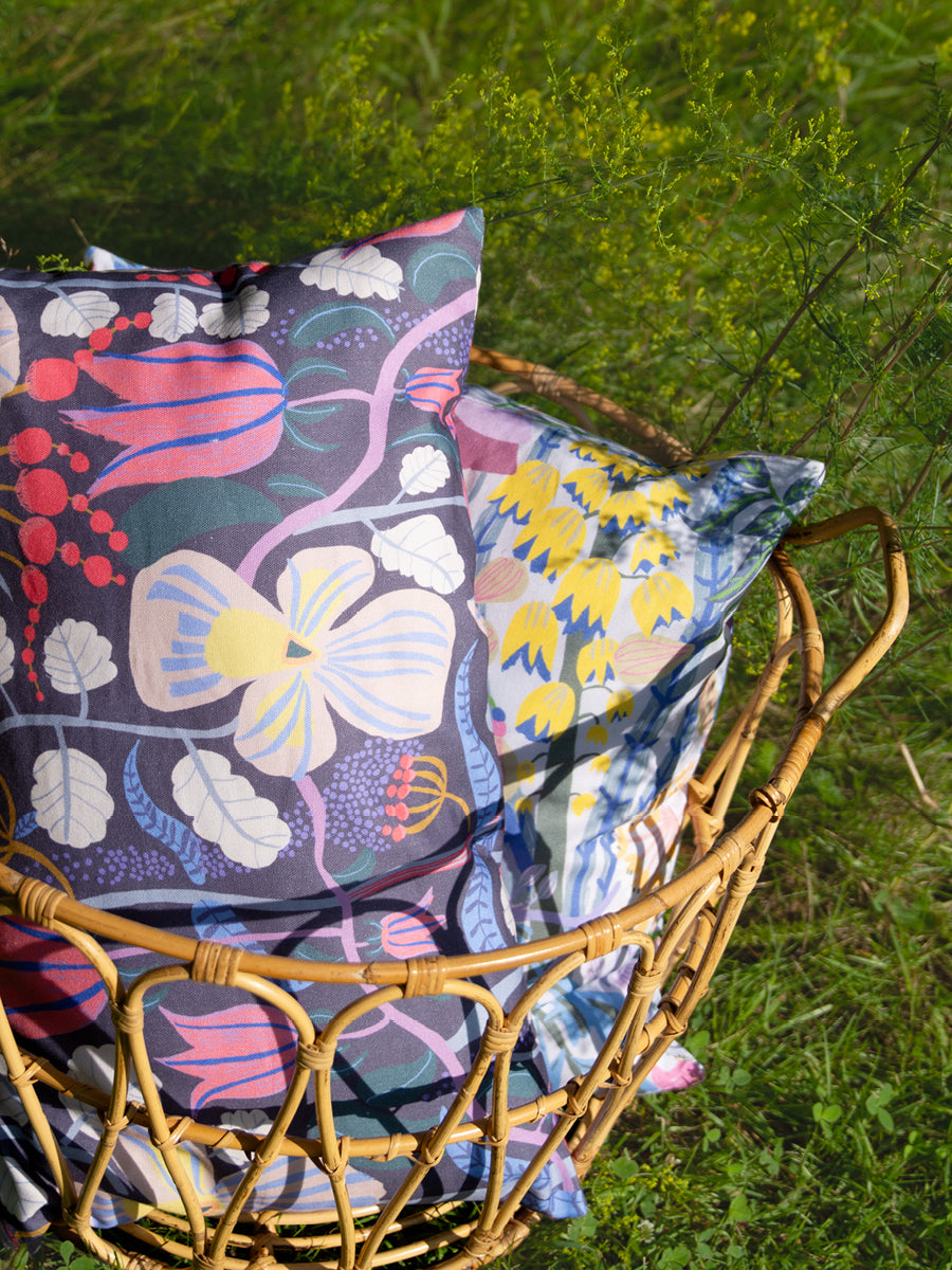 Två mönstrade blommiga kuddar i en krog i trädgården i gröngräset